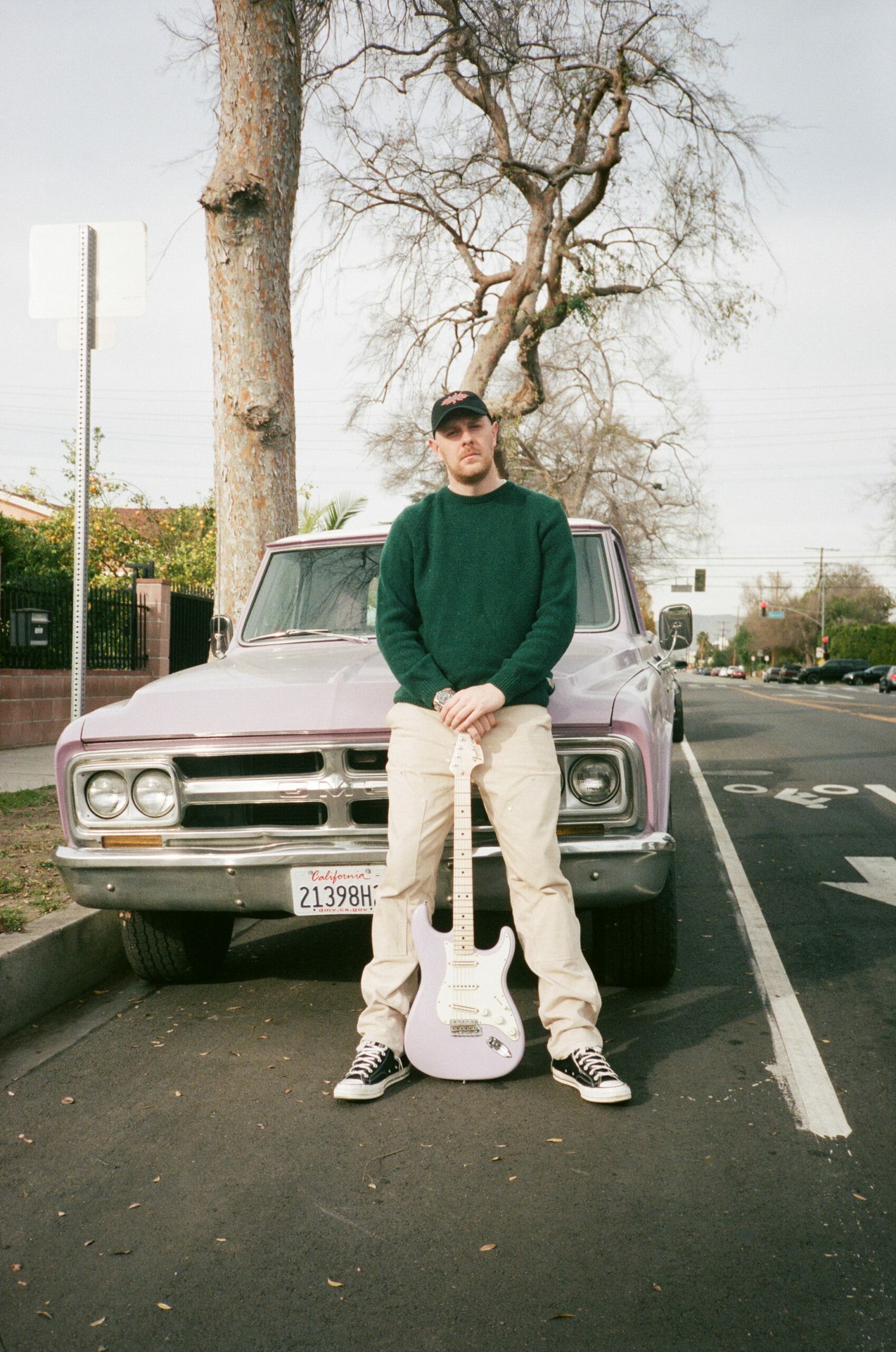 Kenny Beats in front of car with a guitar.